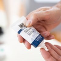 Hände drücken eine Tube Creme aus