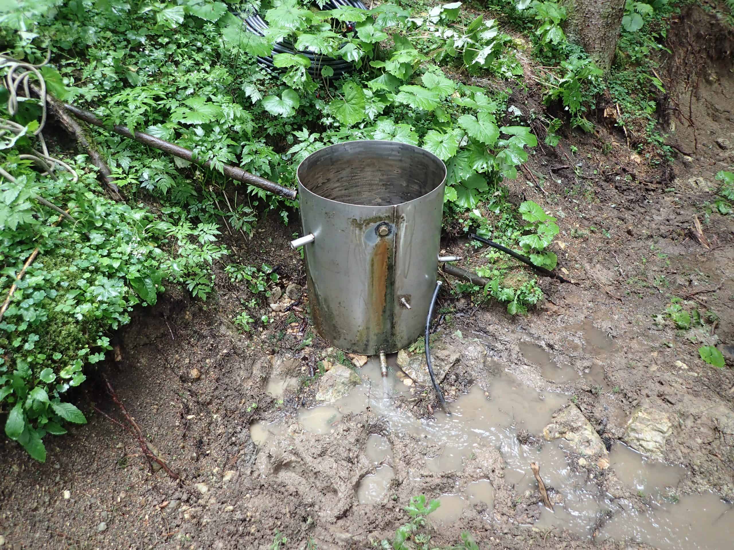 Metallbehälter im Wald mit Wasseransammlung.
